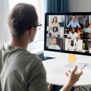 View from back above male shoulder on the laptop with diverse employees, coworkers on the screen, video call, online meeting. App for video conference with many people together