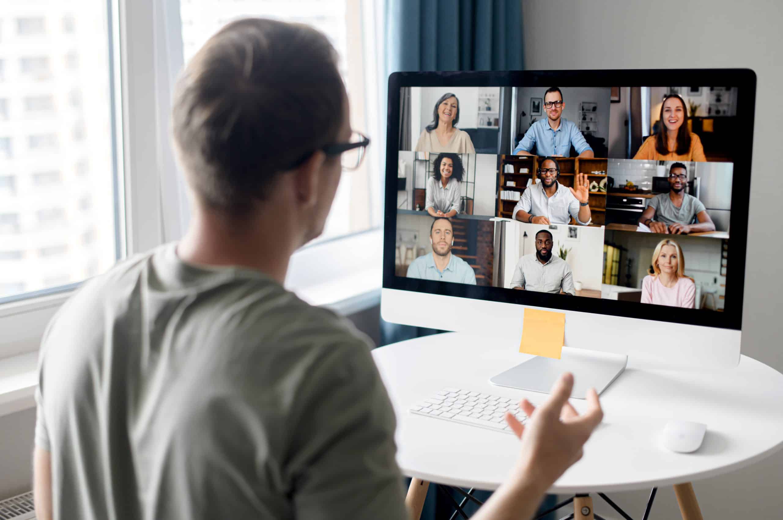 View from back above male shoulder on the laptop with diverse employees, coworkers on the screen, video call, online meeting. App for video conference with many people together